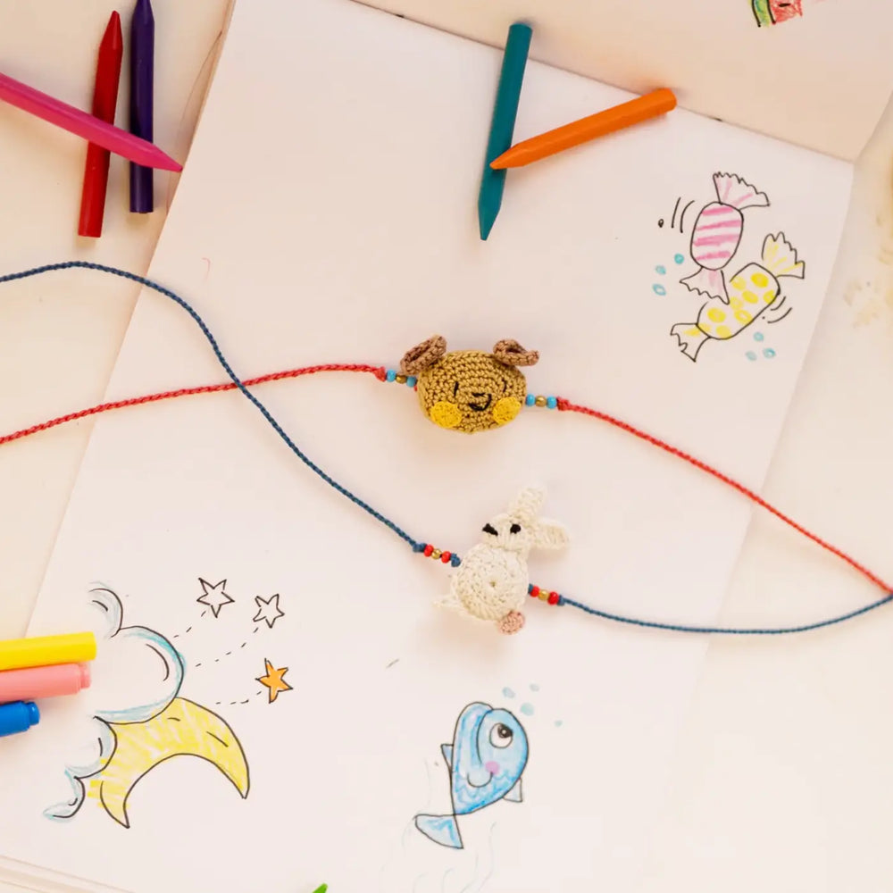 Handmade Crochet Bear And Rabbit Theme Kids Rakhi With Roli Chawal Set Of 2 - Flat Lay with Colored Pencils and Drawings