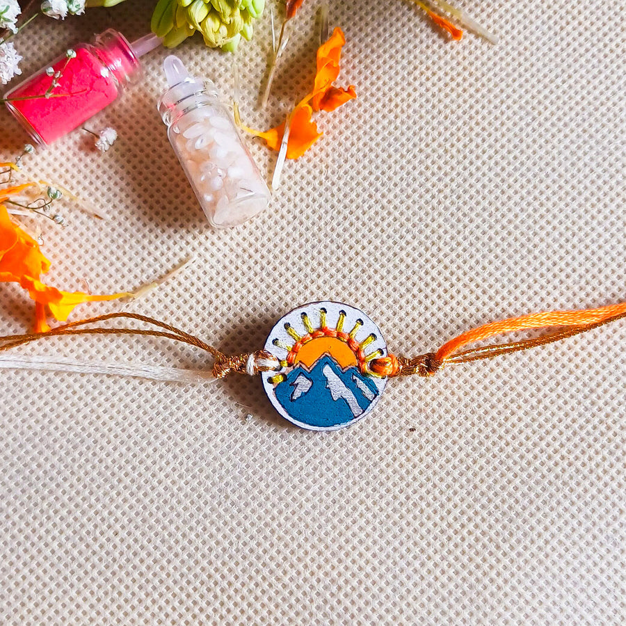 Handmade Mountain And Sun Wooden Rakhi With Roli Chawal For Brother - Top View with Background Elements