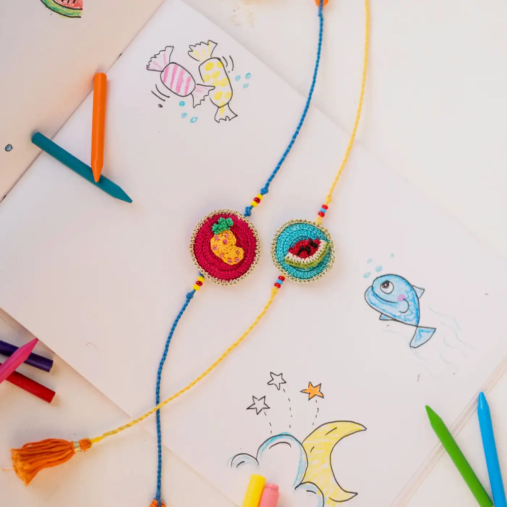 Handmade Crochet Fruits Theme Kids Rakhi With Roli Chawal Set Of 2 - Styled Flat Lay with Art Supplies