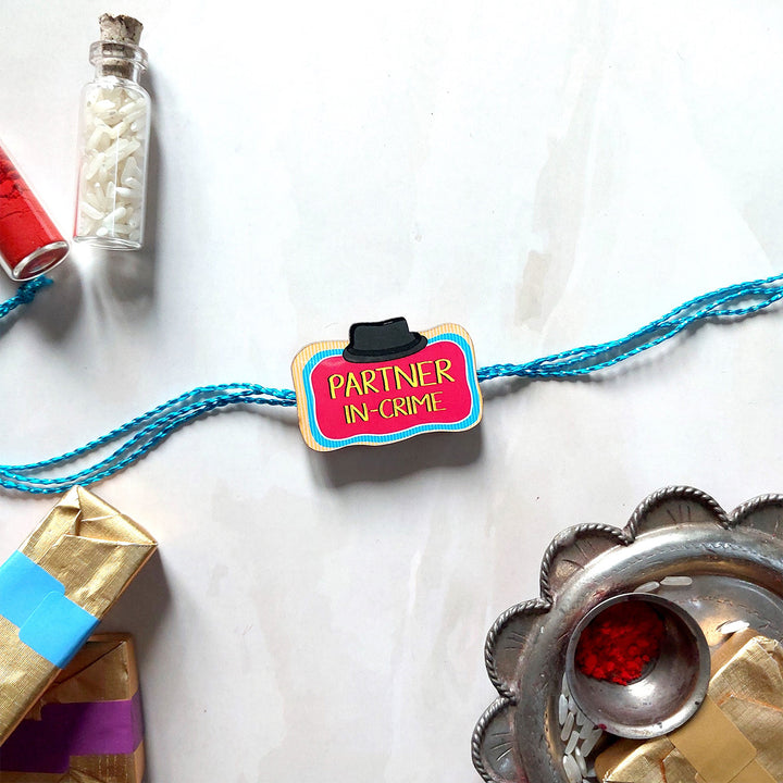 Glossy Printed Wooden 'Partner In Crime' Rakhi With Kumkum Rice For Brother