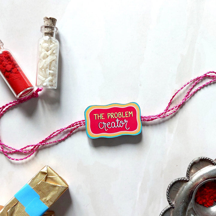 Glossy Printed Wooden 'Problem Creator' Rakhi With Kumkum Rice For Brother