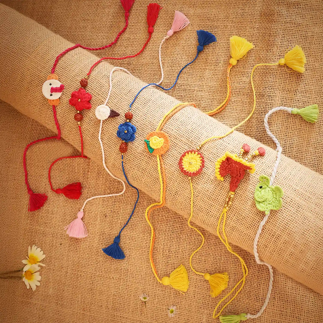 Handmade Crochet Multicolor Family Rakhi With Roli Chawal Set Of 8 - Flat lay with floral decoration