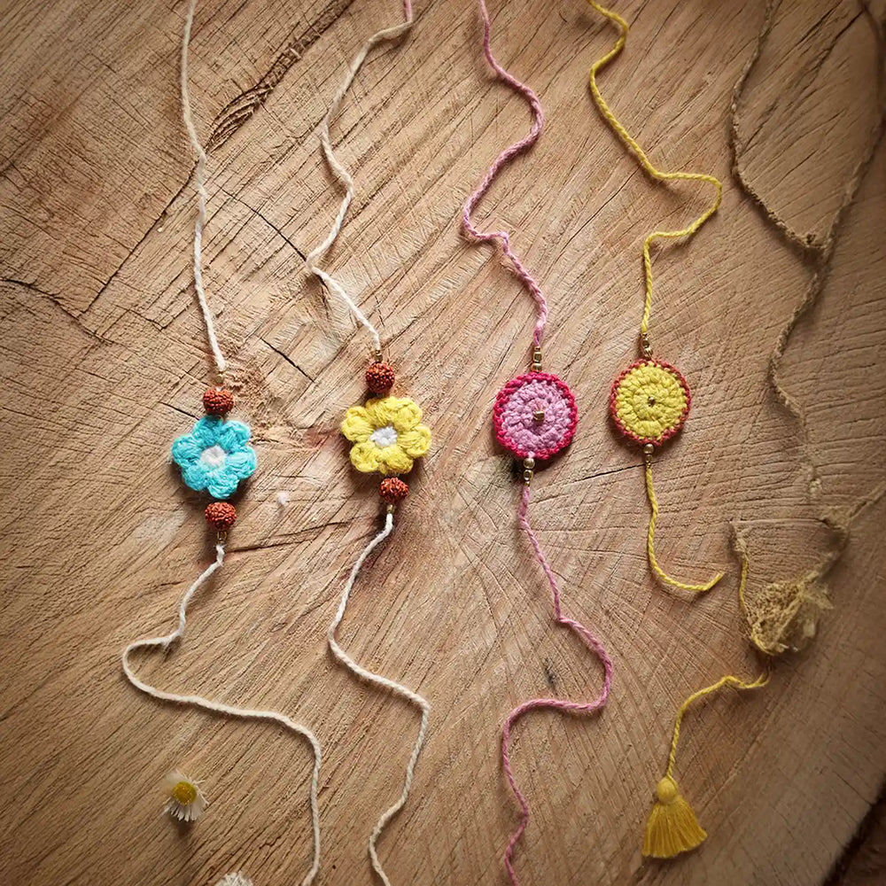 Handmade Crochet Pink Yellow And Blue Rudraksh Rakhi With Roli Chawal Set Of 4 - Flat lay on wood surface