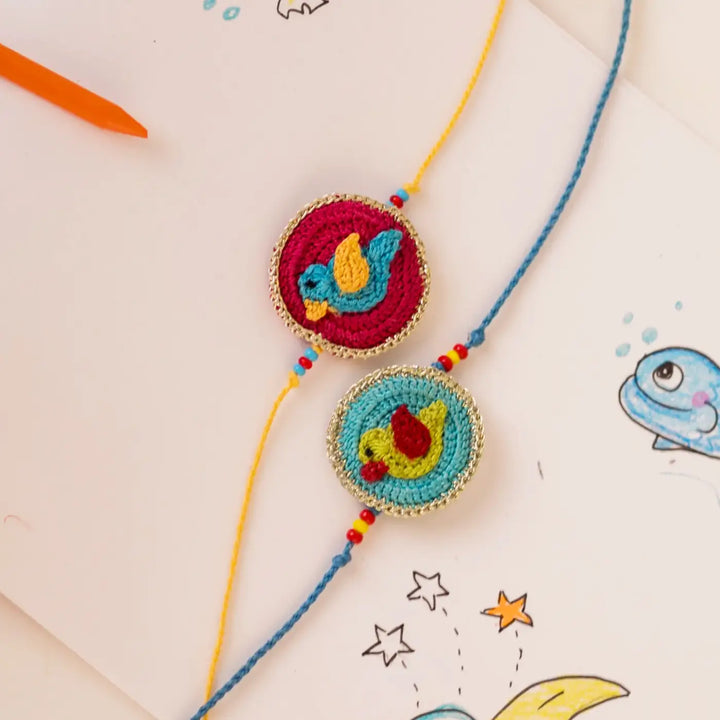 Handmade Crochet Birds Theme Kids Rakhi With Roli Chawal Set Of 2 - Detailed View on Sketchbook Background