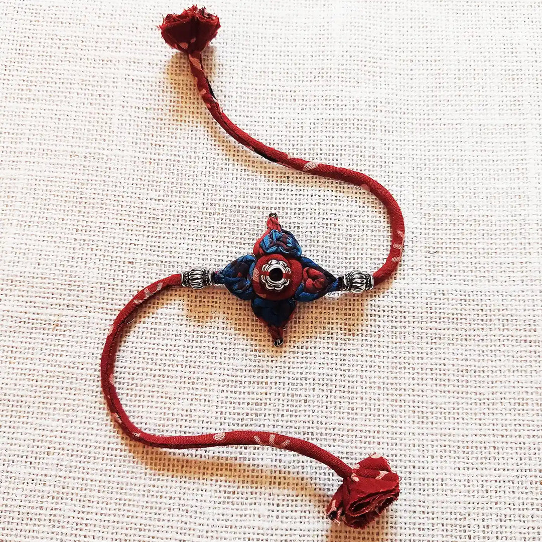 Handmade Dori Work Flower Ajrakh Rakhi With Roli Chawal - Full Product Display on Fabric