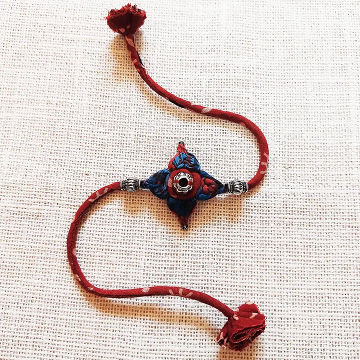 Handmade Dori Work Flower Ajrakh Rakhi With Roli Chawal - Full Product Display on Fabric