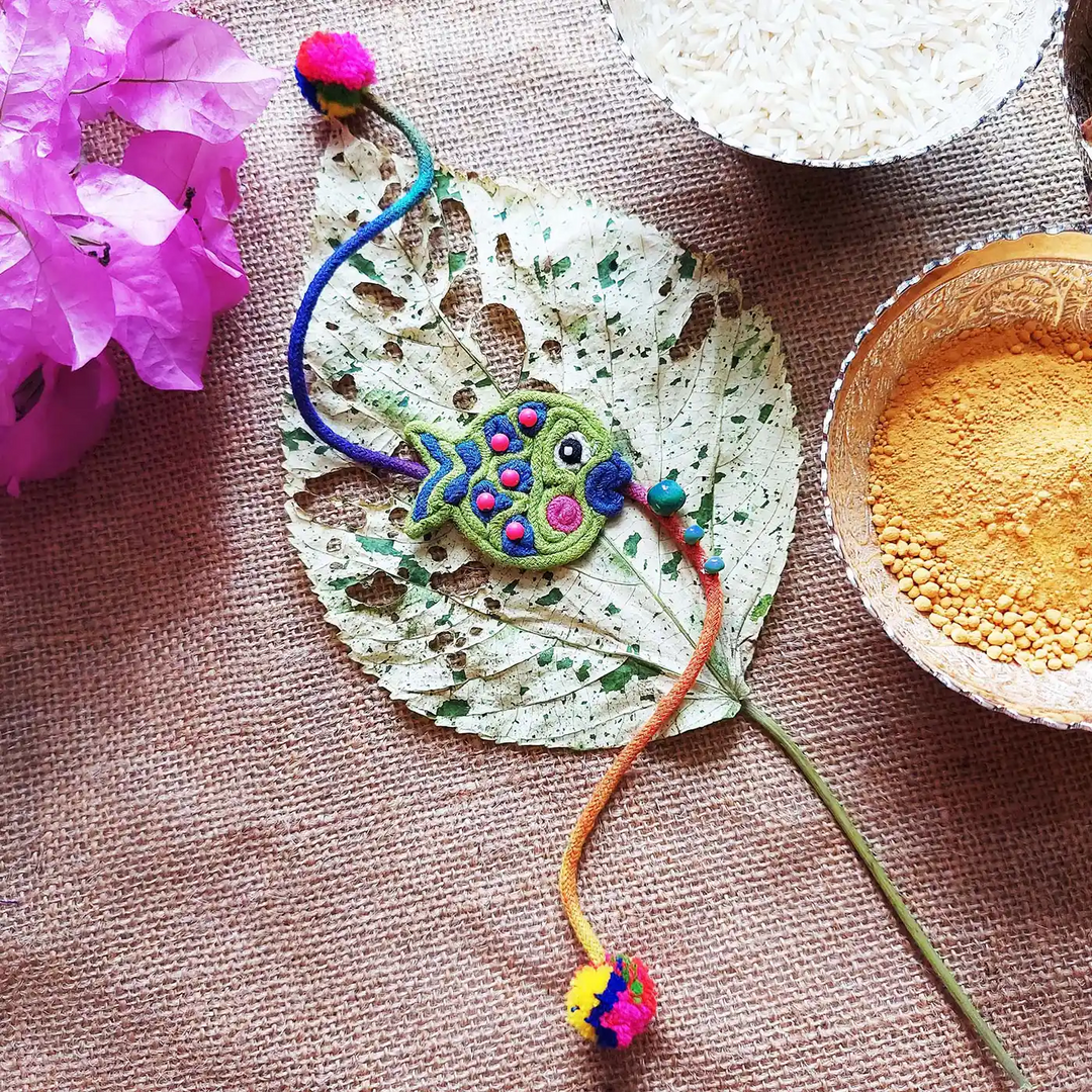 Handmade Dori Work Beaded Cute Fish Kids Rakhi With Roli Chawal - Flat Lay with Decorative Props
