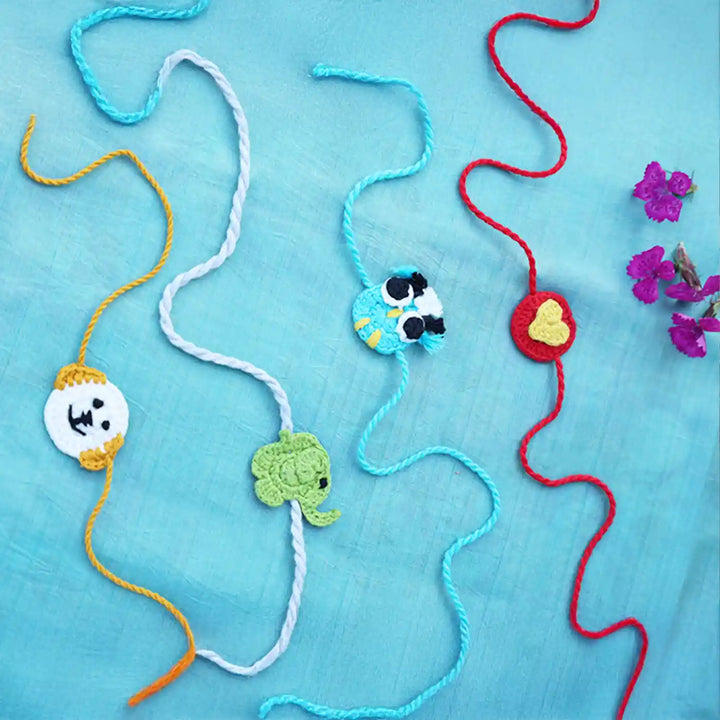 Handmade Crochet Owl Elephant Dog And Heart Kids Rakhi With Roli Chawal Set Of 4 - Laid Out on Blue Background