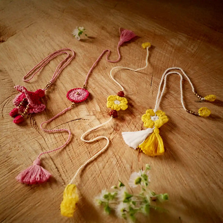 Handmade Crochet Pink And Yellow Bhaiya Bhabhi Rakhi With Roli Chawal Set Of 4 - Angled Flat Lay with Floral Accent