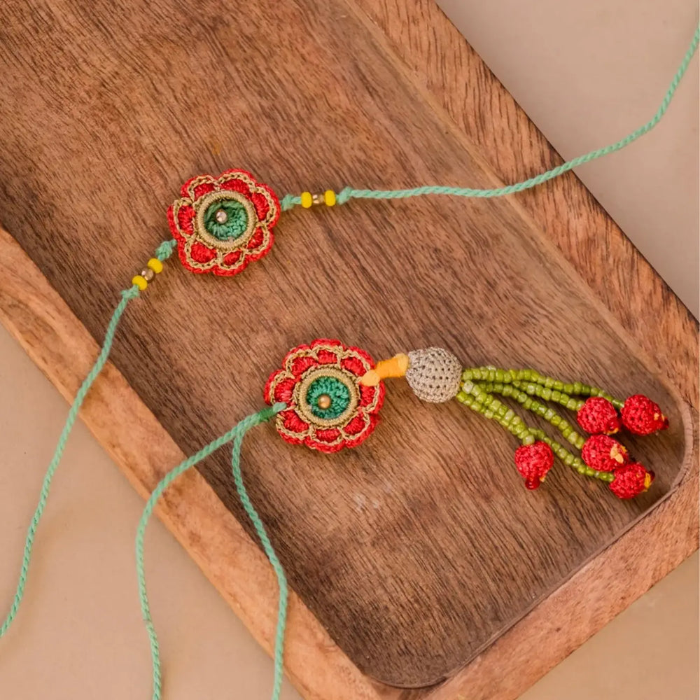 Handmade Crochet Green And Red Flower Bhaiya Bhabhi Rakhi With Roli Chawal Set Of 2 - Top view on wooden tray