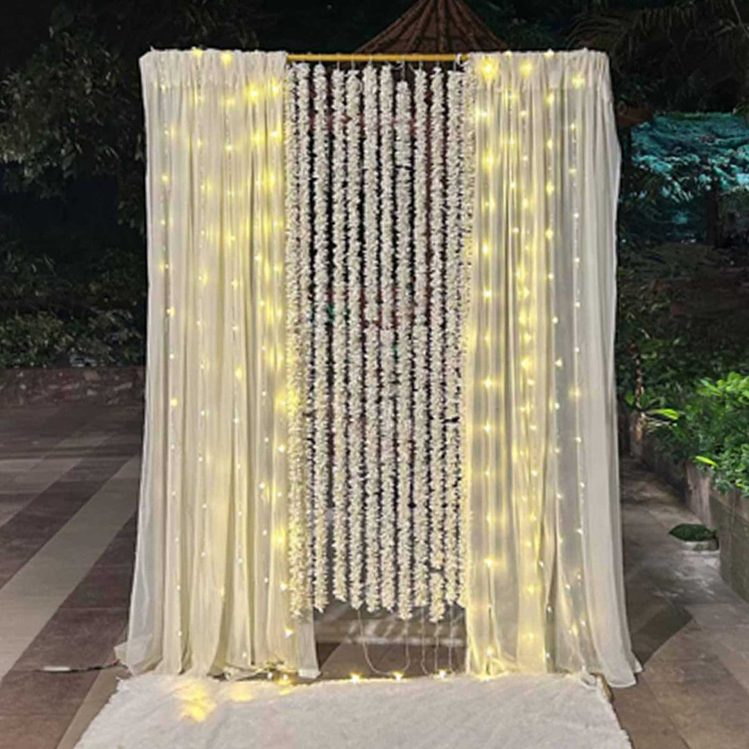 White Floral Garland Backdrop Decor Kit With Off-White Crepe Curtains & Fairy Lights For Weddings
