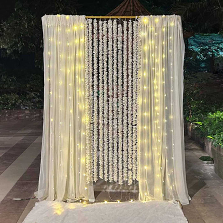 White Floral Garland Backdrop Decor Kit With Off-White Crepe Curtains & Fairy Lights For Weddings