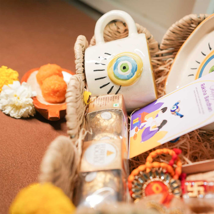 Personalized Handmade Evil Eye Design Guardians Blessing Rakhi Hamper Includes 1 Basket 1 Cup And Saucer 1 Rakhi 1 Roli Chawal And 1 Message Card - Close-up of basket contents