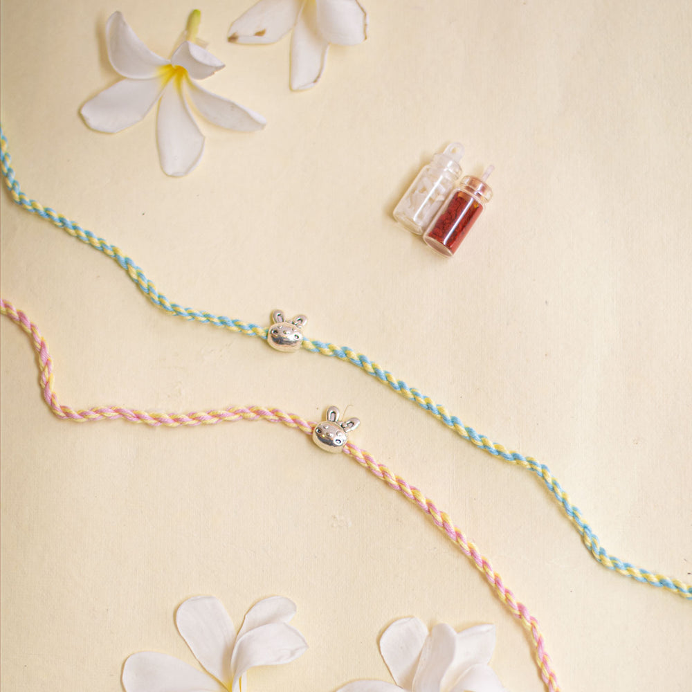Handmade Silver Bunny Design Kids Rakhi With Roli Chawal - Flat lay with flowers and charms