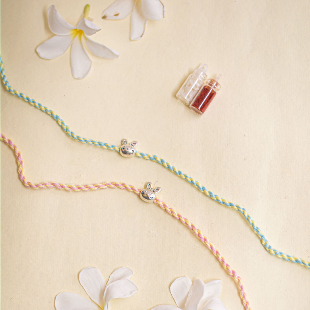 Handmade Silver Bunny Design Kids Rakhi With Roli Chawal - Flat lay with flowers and charms