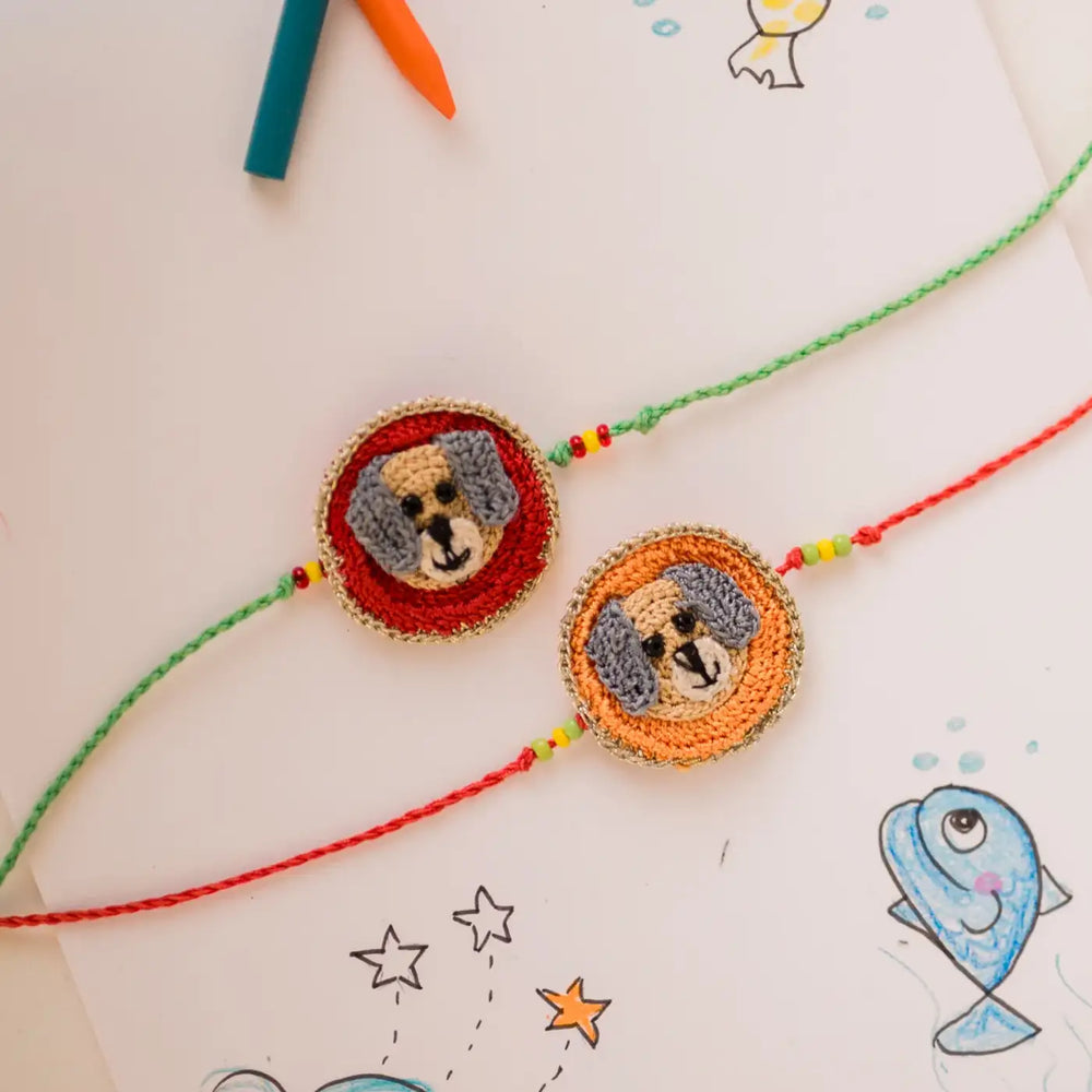 Handmade Crochet Dog Theme Kids Rakhi With Roli Chawal Set Of 2 - Top view with surrounding sketchbook