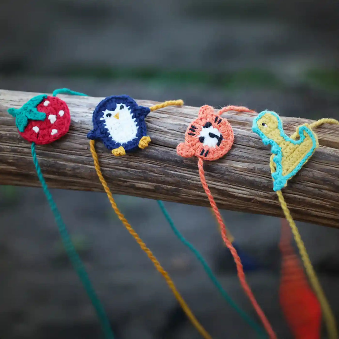 Handmade Crochet Dino Tiger Strawberry And Penguin Kids Rakhi With Roli Chawal Set Of 4 - Front View Display on Wood