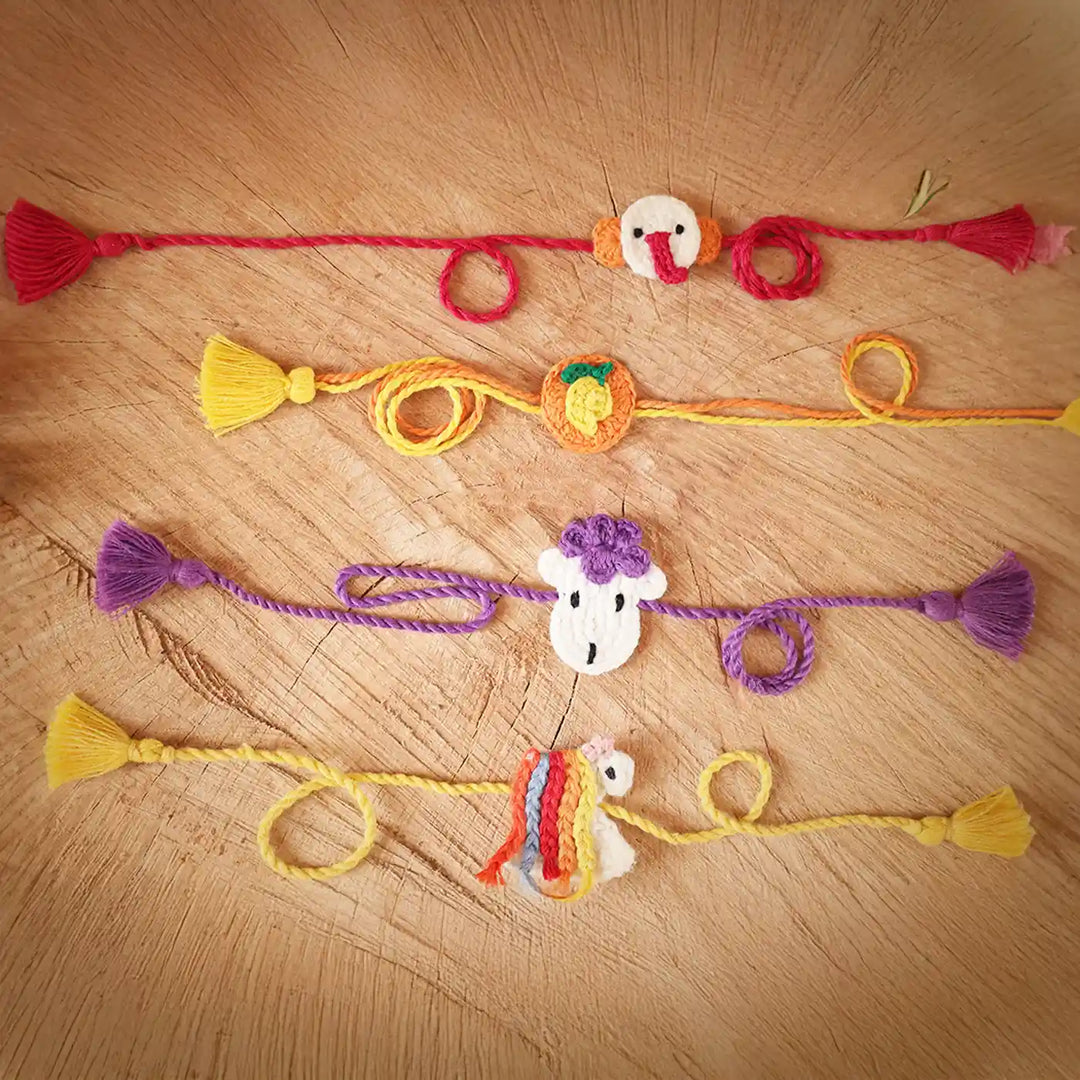 Handmade Crochet Ganesha Mango Sheep And Unicorn Kids Rakhi With Roli Chawal Set Of 4 - Laid Flat with Tassels Visible