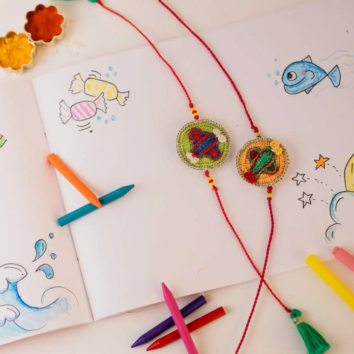 Handmade Crochet Airplane Theme Kids Rakhi With Roli Chawal Set Of 2 - Styled Display with Crayons
