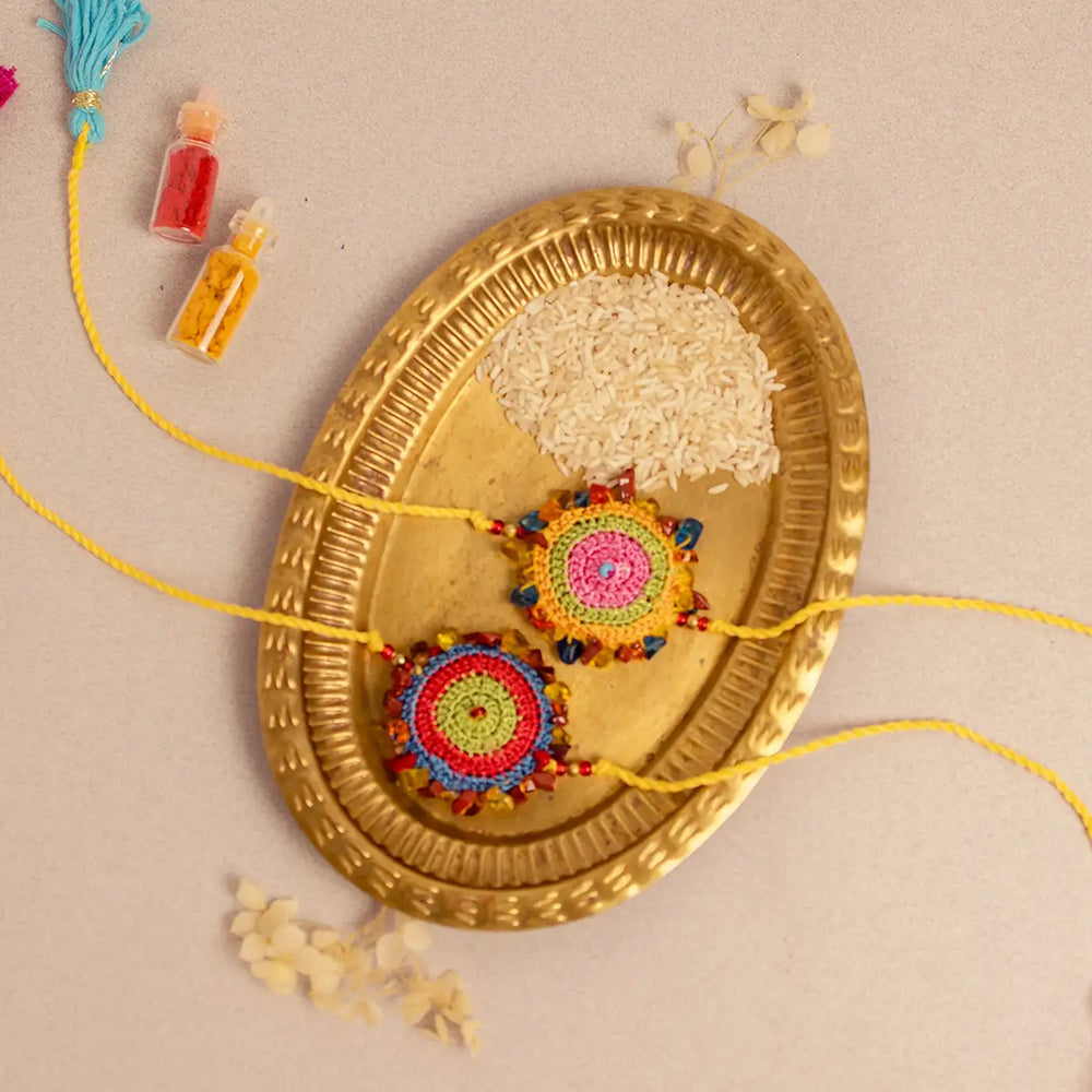 Handmade Crochet Multicolor Dhanak Rakhi With Roli Chawal Set Of 2 - Top View on Brass Plate