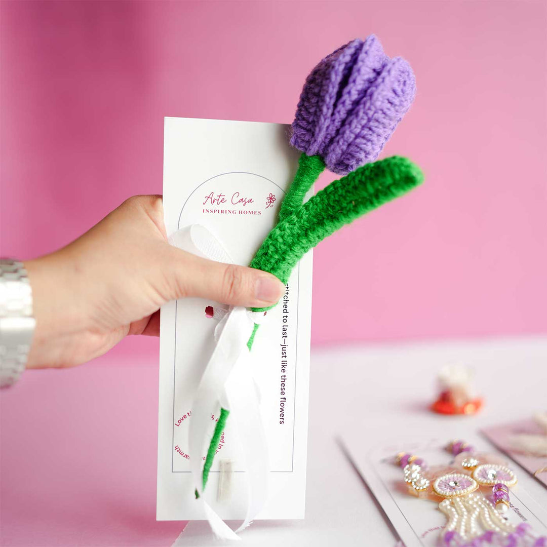 Personalized Handmade Crochet Tulip Dark Purple Rakhi Hamper Includes 1 Crochet Flower 1 Message Card And 2 Rakhis And Roli Chawal - Hand Holding Product with Tag