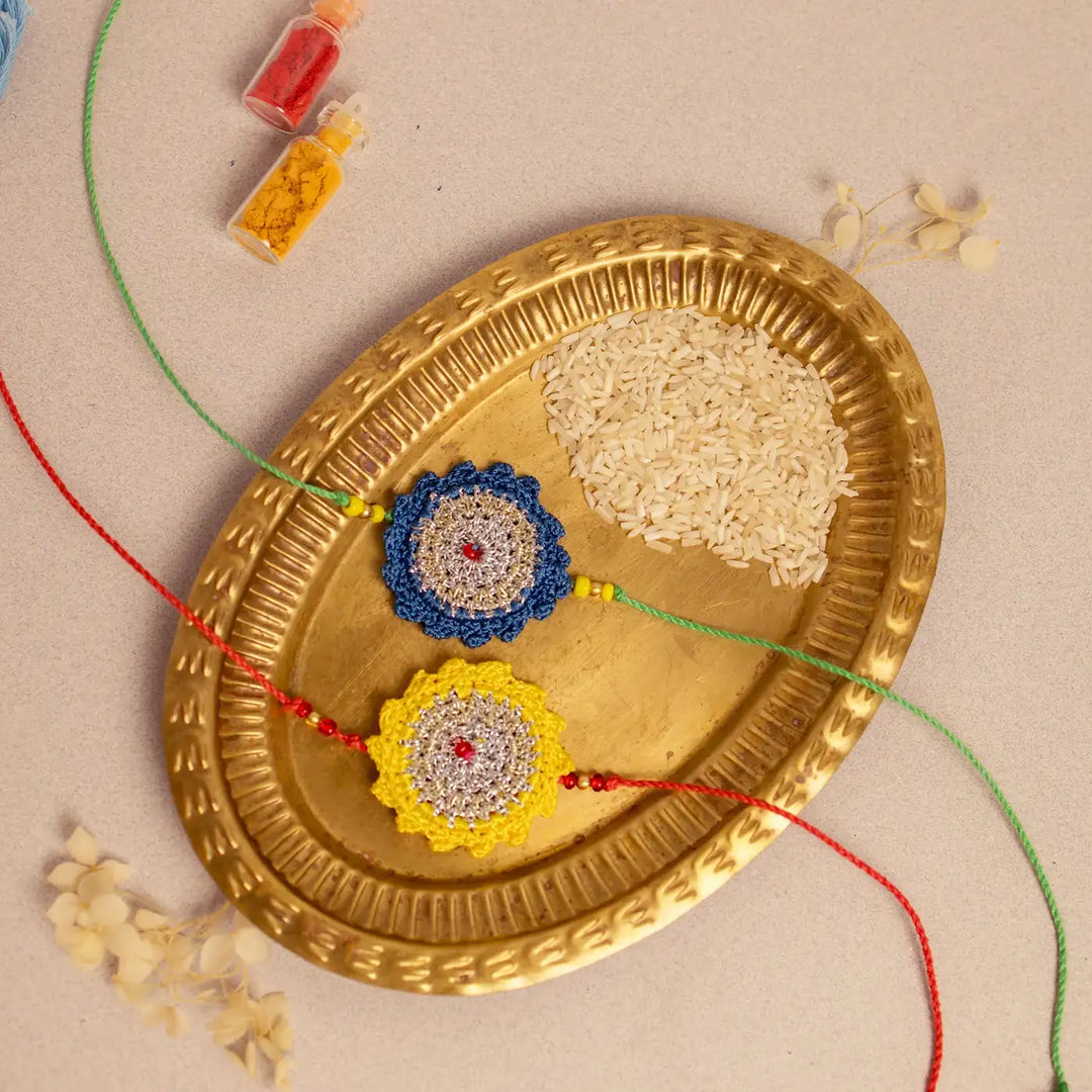 Handmade Crochet Blue And Yellow Seher Rakhi With Roli Chawal Set Of 2 - Angled view showing full rakhi strings