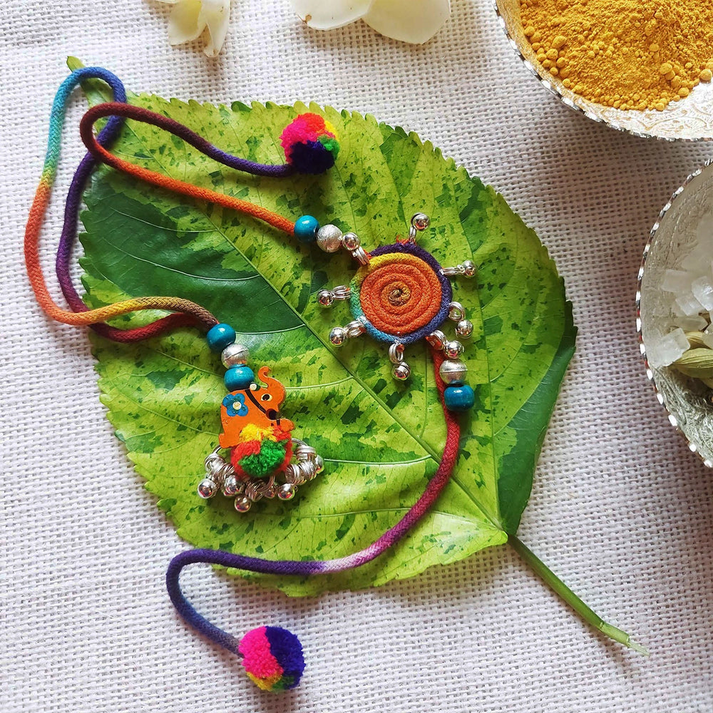Handmade Dori Work Elephant And Ghungroo Bhaiya Bhabhi Rakhi With Roli Chawal Set Of 2 - Decorative elements on green leaf background