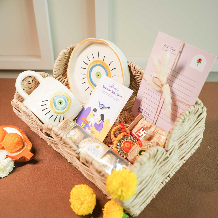 Personalized Handmade Evil Eye Design Guardians Blessing Rakhi Hamper Includes 1 Basket 1 Cup And Saucer 1 Rakhi 1 Roli Chawal And 1 Message Card - Angled basket with contents visible