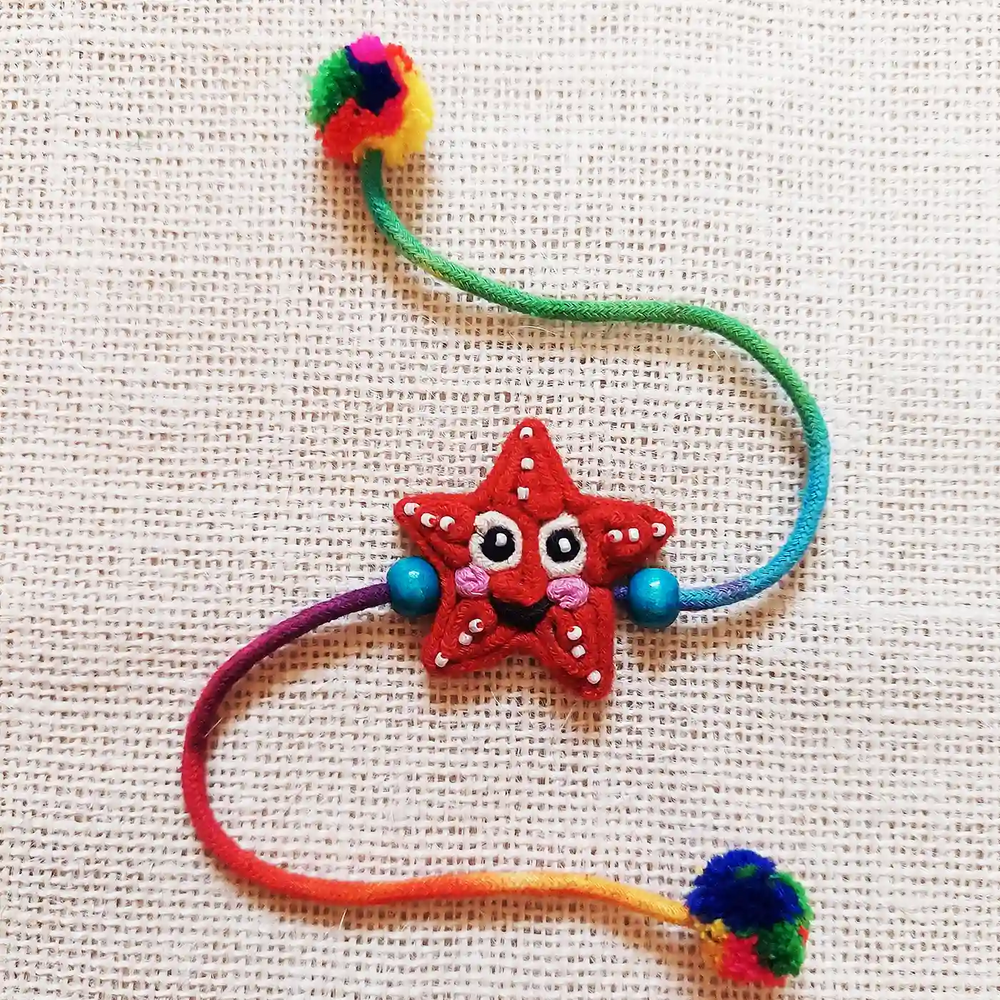 Handmade Dori Work Starfish Kids Rakhi With Roli Chawal - Top View on Textured Surface
