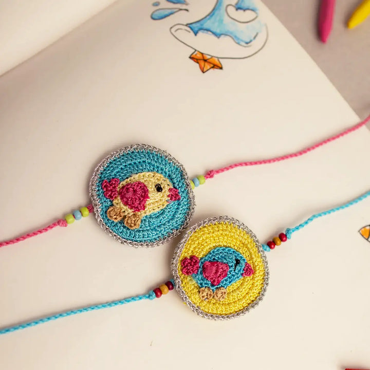 Handmade Crochet Bird Theme Kids Rakhi With Roli Chawal Set Of 2 - Close-up Front View with Sketchbook