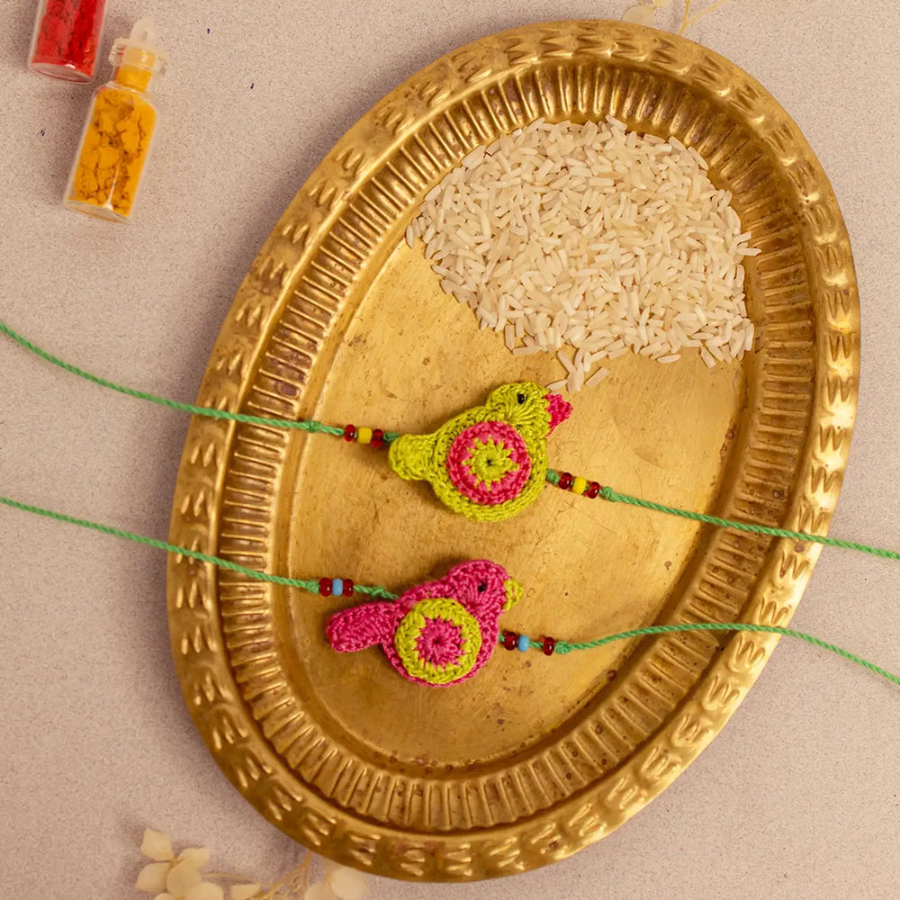 Handmade Crochet Green And Pink Birds Rakhi With Roli Chawal Set Of 2 - Top View with Decorative Plate