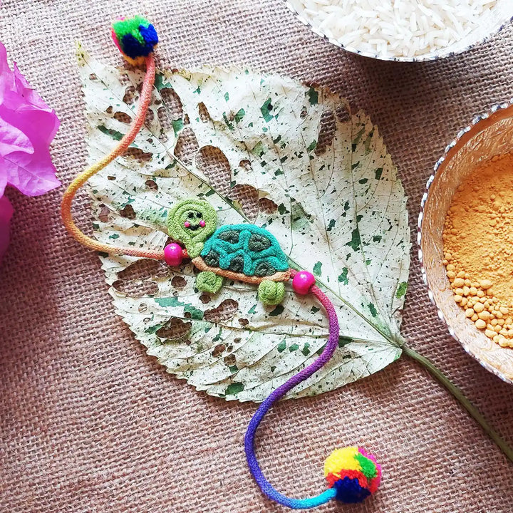 Handmade Dori Work Cute Tortoise Kids Rakhi With Roli Chawal - Styled Flat Lay Display