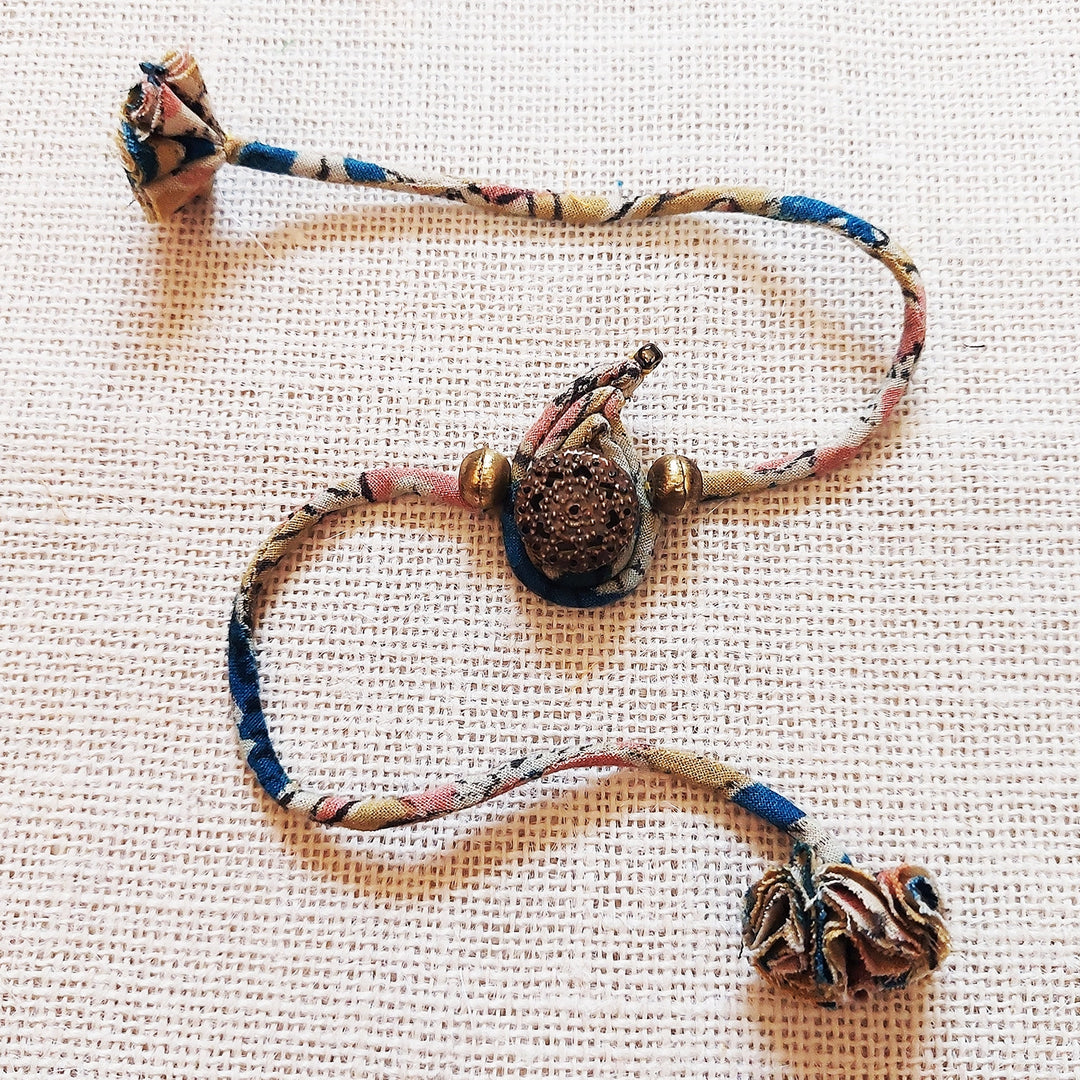 Handmade Dori Work Ambi Kalamkari Rakhi With Roli Chawal - Flat Lay on Fabric Background