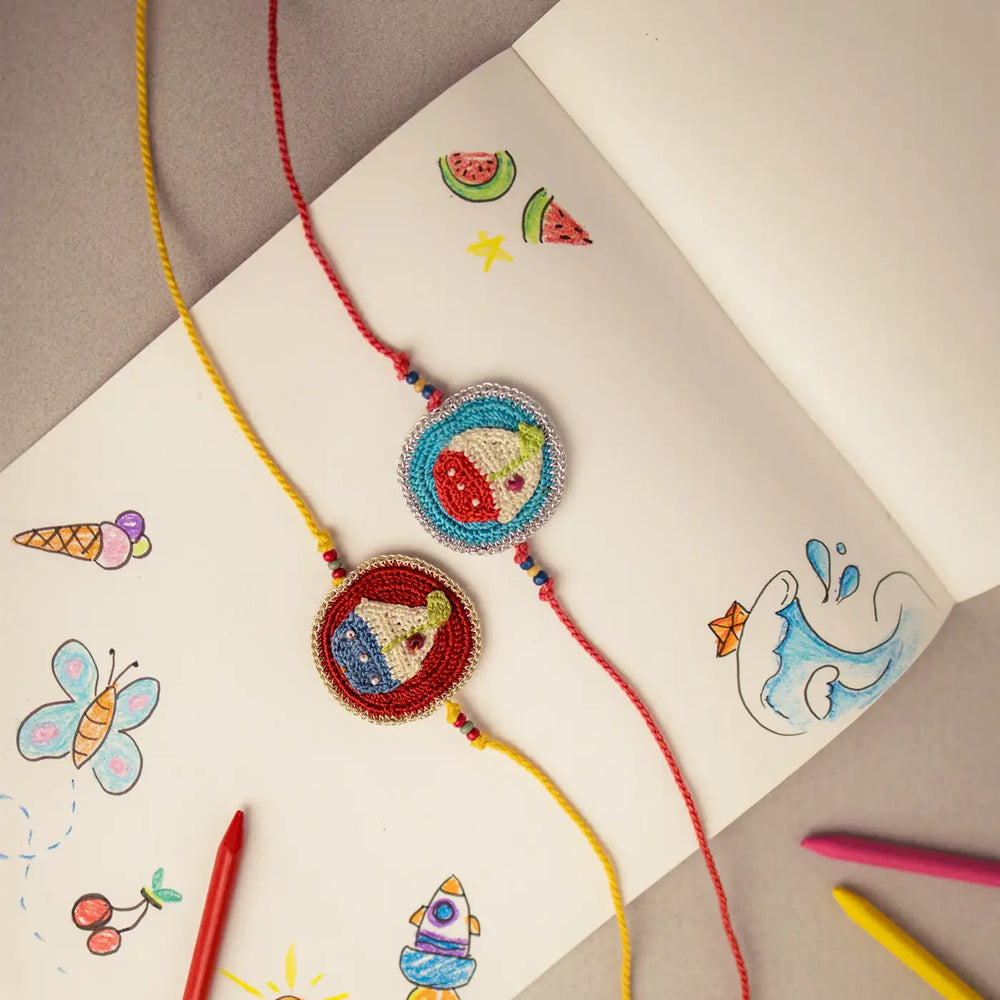 Handmade Crochet Boat Theme Kids Rakhi With Roli Chawal Set Of 2 - Top View of Bracelets on Paper