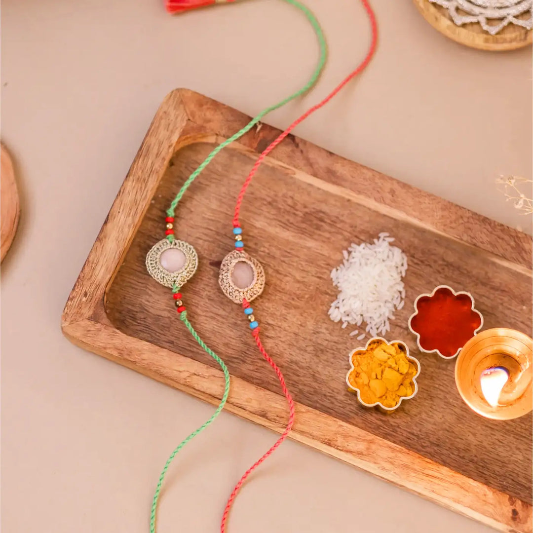 Handmade Crochet Moon Shine Rakhi With Roli Chawal Set Of 2 - Styled Flat Lay with Lit Diya