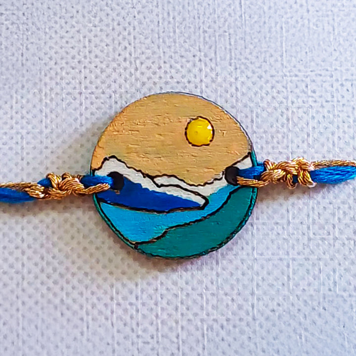 Handmade Mountain Sun And Snow Wooden Rakhi With Roli Chawal For Brother - Close-up Front View with Blue Thread
