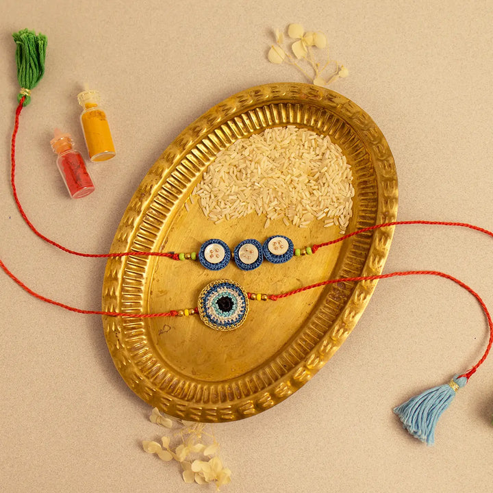 Handmade Crochet Noor And Nazar Evil Eye Rakhi With Roli Chawal Set Of 2 - Styled flat lay with accessories