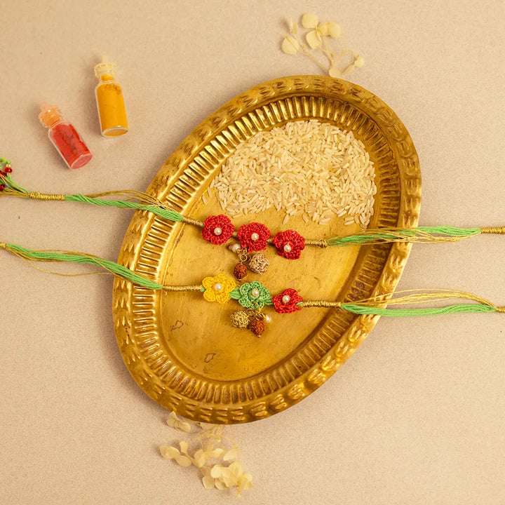 Handmade Crochet Ananya Phool And Rudraksh Rakhi With Roli Chawal Set Of 2 - Flat Lay of Rakhis and Rice