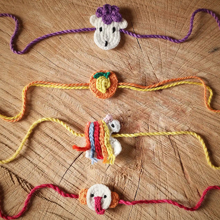 Handmade Crochet Ganesha Mango Sheep And Unicorn Kids Rakhi With Roli Chawal Set Of 4 - Laid Flat on Wooden Surface