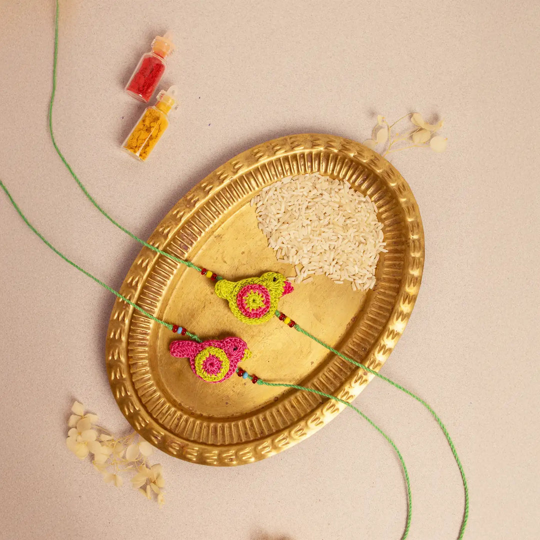 Handmade Crochet Green And Pink Birds Rakhi With Roli Chawal Set Of 2 - Angled View with Decorative Elements