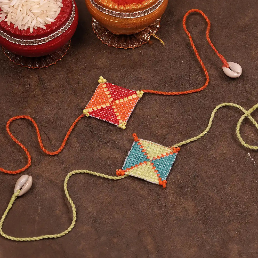Hand Embroidered Cross Knot Rakhi With Roli Chawal Set Of 2 - Styled Flat Lay with Bowls