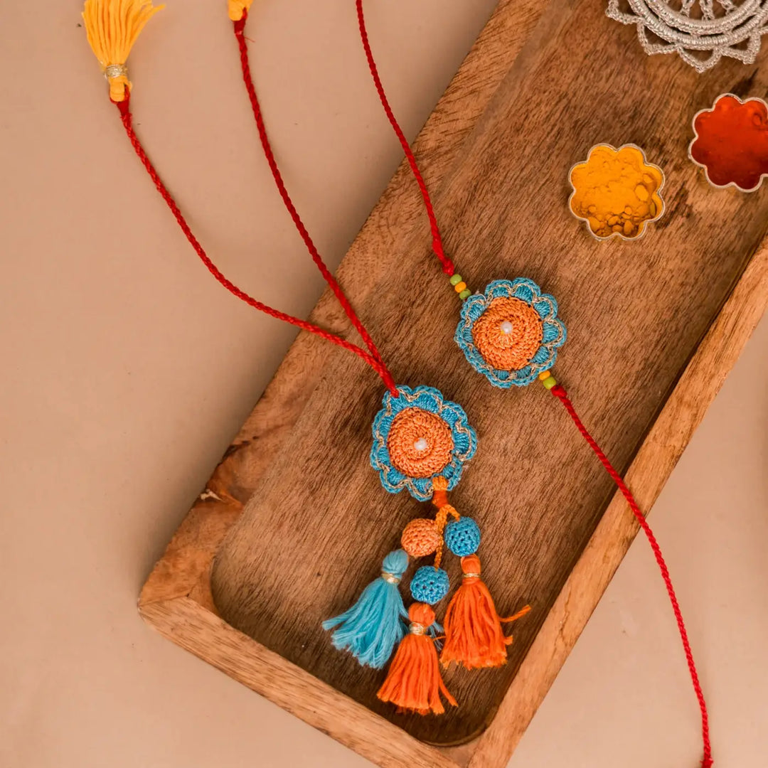 Handmade Crochet Blue And Orange Camelia Bhaiya Bhabhi Rakhi With Roli Chawal Set Of 2 - Overhead View with Tray and Decorations