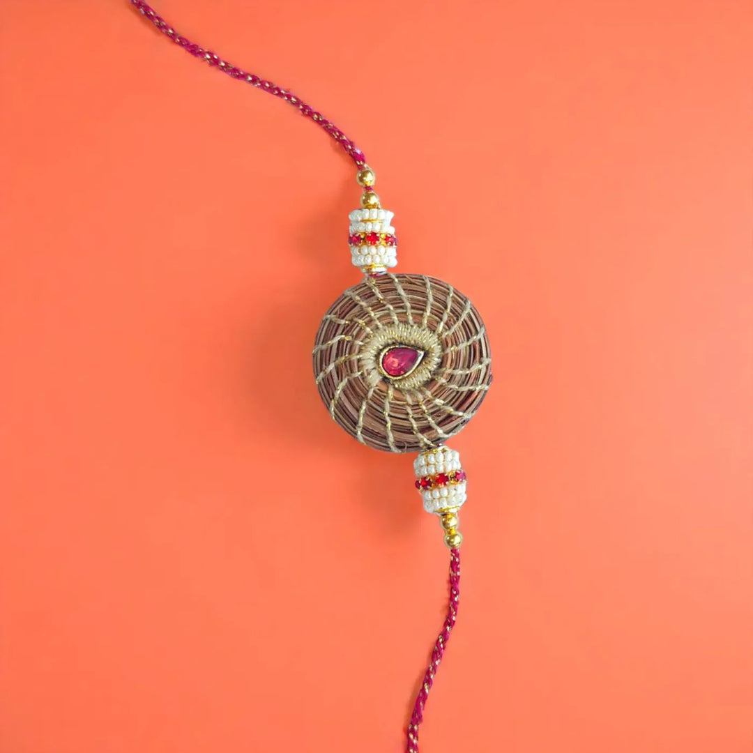 Eco Friendly Handmade Red Stone Pine Needle Rakhi With Pouch And Roli Chawal - Flat Lay on Orange Background