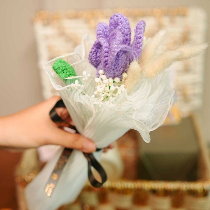 Personalized Handmade Crochet Evil Eye Theme Rakhi Hamper Includes 1 Basket 1 Mug 1 Candle 1 Crochet Flower 2 Rakhis 1 Roli Chawal And 1 Message Card - Holding Purple Crochet Tulip Flowers