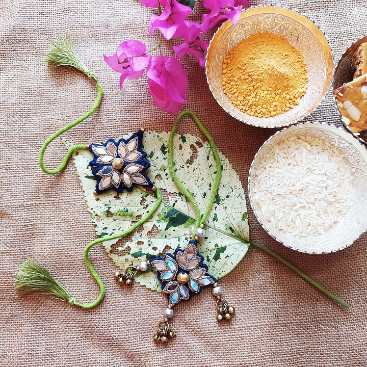 Handmade Mirror Work And Ghungroo Blue Bhaiya Bhabhi Rakhi With Roli Chawal Set Of 2 - Styled Flat Lay with Background Props