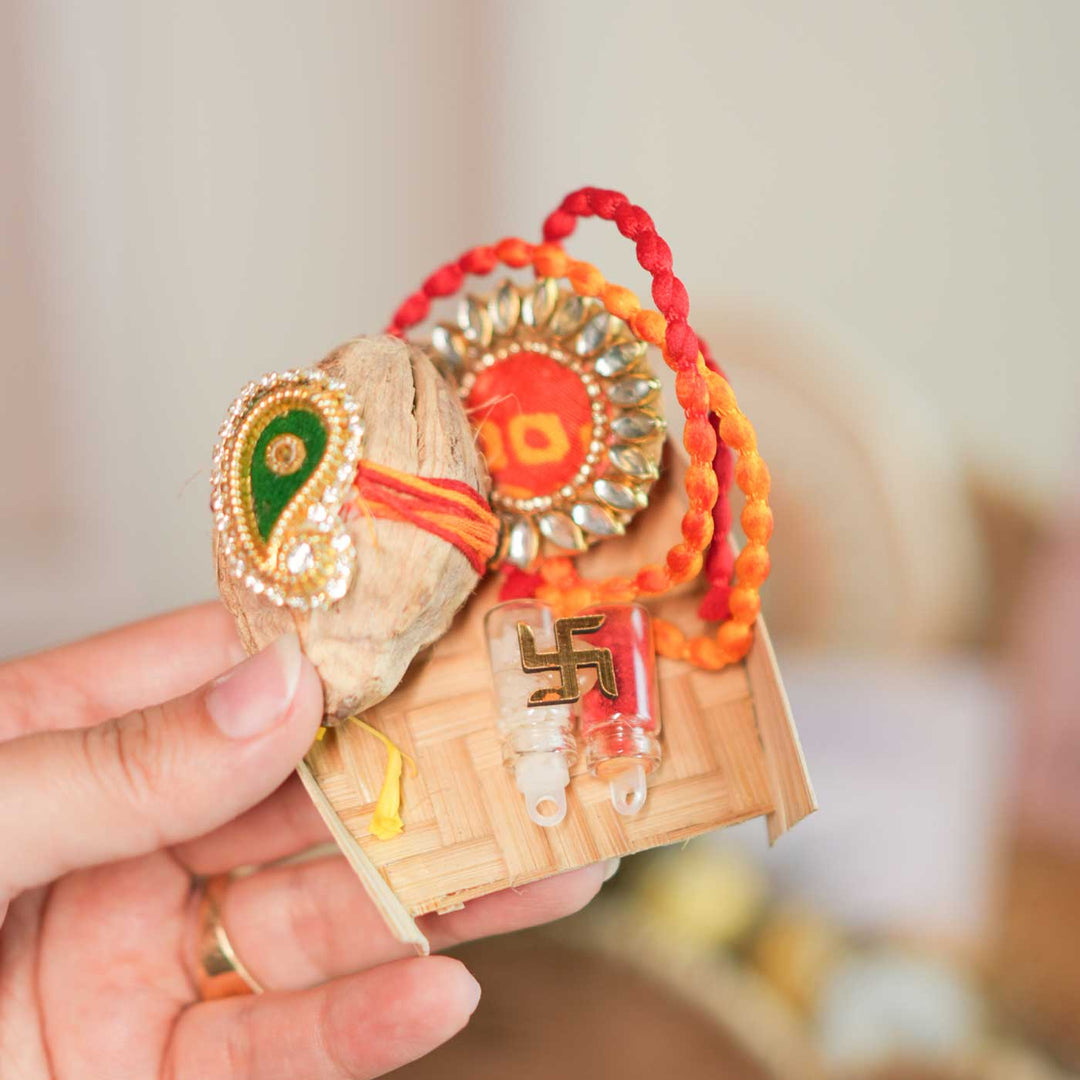 Personalized Handmade Evil Eye Design Guardians Blessing Rakhi Hamper Includes 1 Basket 1 Cup And Saucer 1 Rakhi 1 Roli Chawal And 1 Message Card - Hand displaying traditional rakhi items