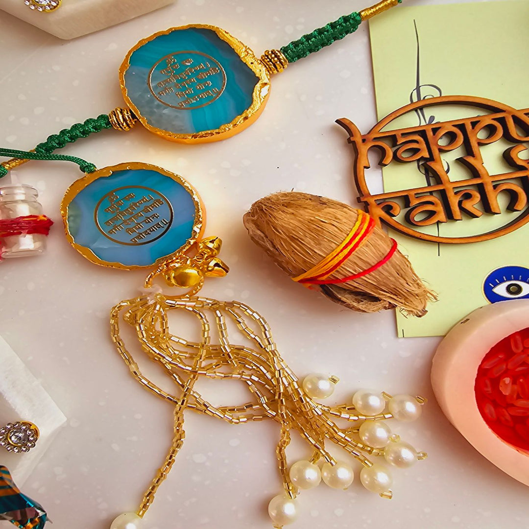 Handmade Gayatri Mantra Agate Bhaiya Bhabhi Rakhi With Roli Chawal - Flat lay of blue Rakhi with traditional items