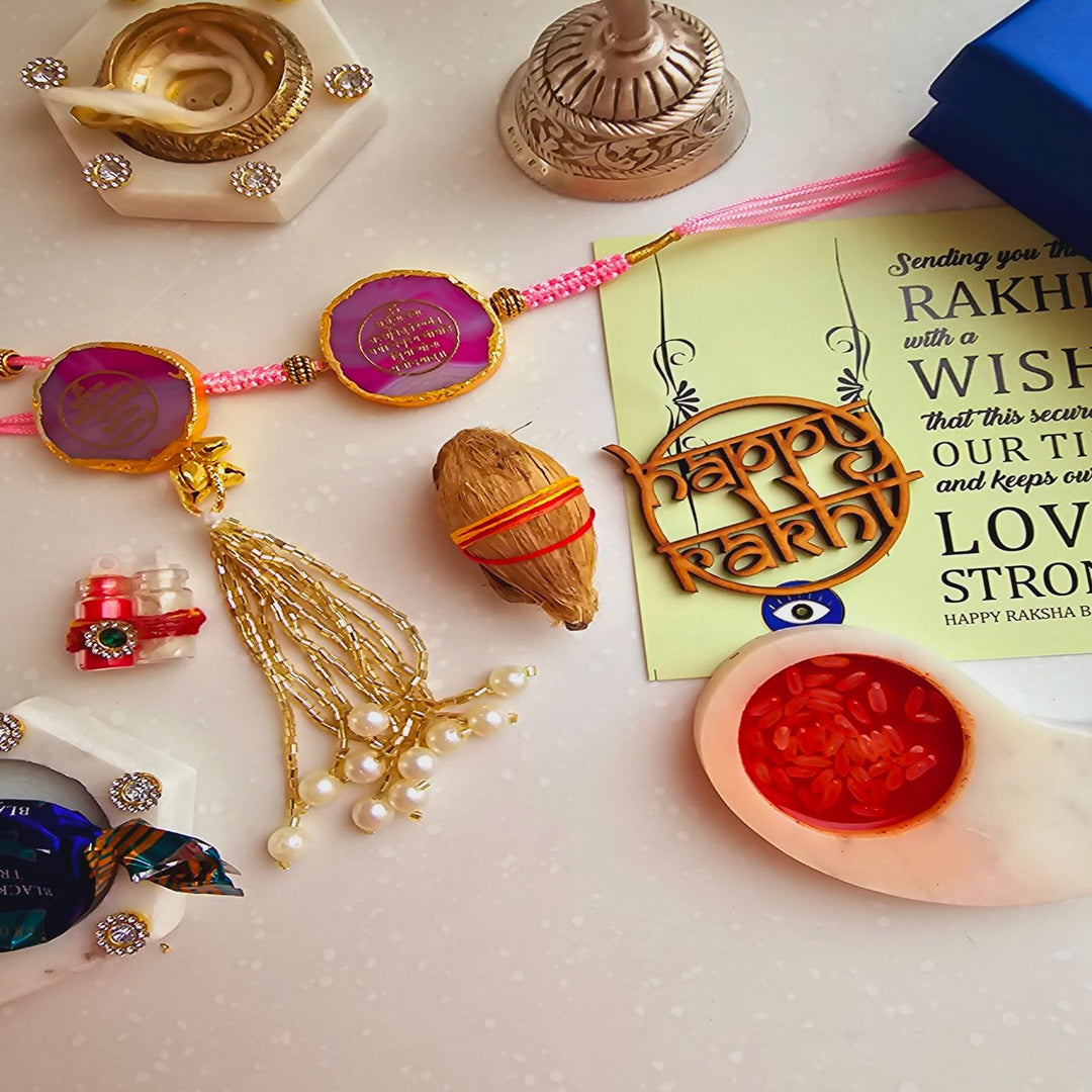 Handmade Gayatri Mantra Agate Bhaiya Bhabhi Rakhi With Roli Chawal - Flat lay of pink Rakhi set and greeting card