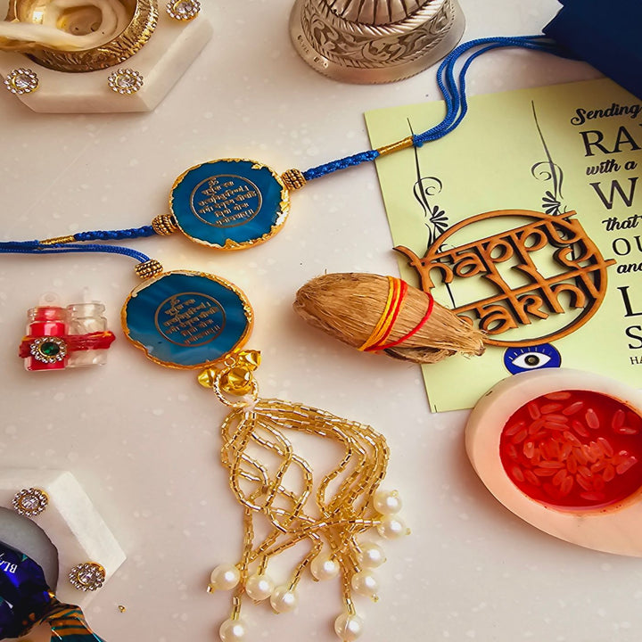 Handmade Gayatri Mantra Agate Bhaiya Bhabhi Rakhi With Roli Chawal - Flat lay of blue Rakhi with festive elements