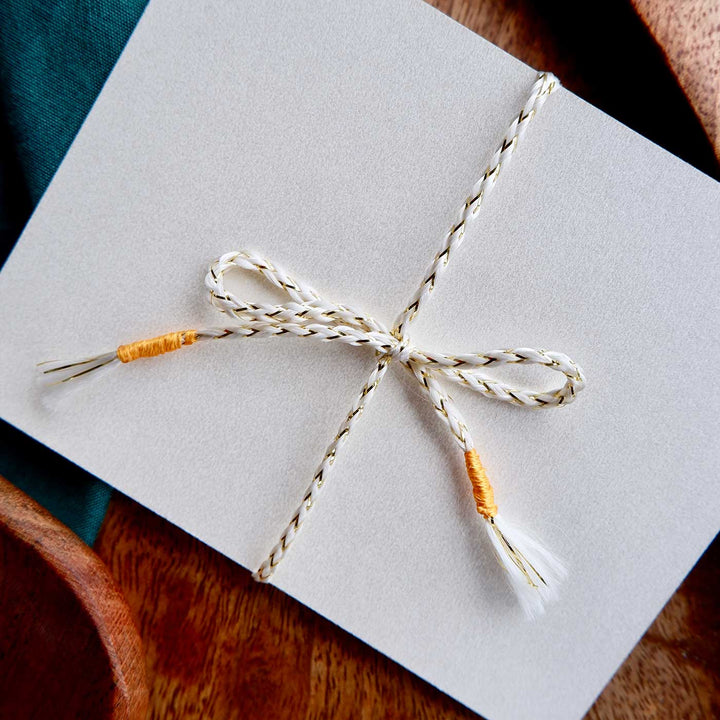 Handmade Zardozi White And Golden Rakhi With Wooden Box And Roli Chawal - Bow Tie Close-up on Paper